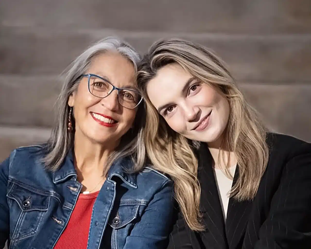 Two women with heads against each other facing the camera smiling